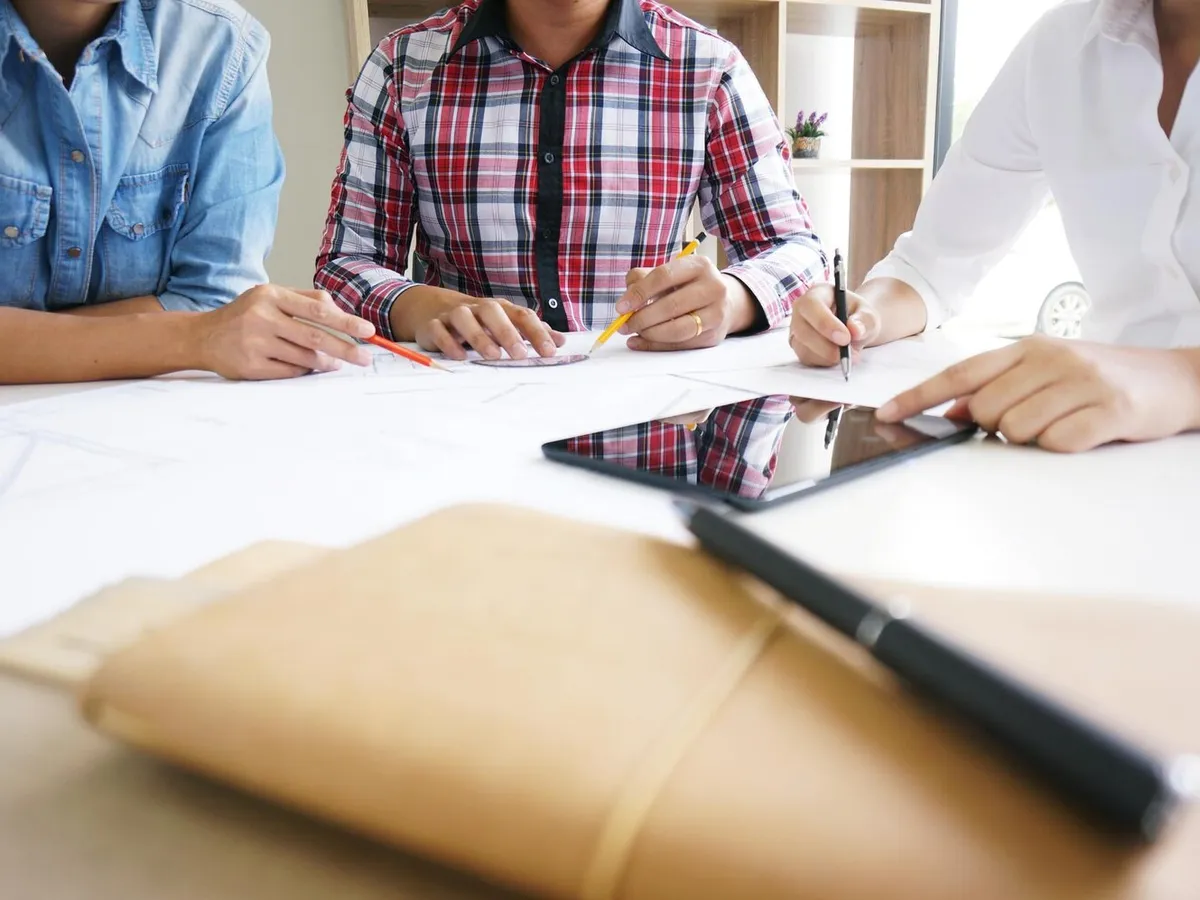 Trois personnes annotent des plans d'immeuble autour d'une table de réunion
